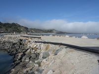view of some sand and rocks on a river and a bridge in the foreground