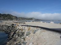 view of some sand and rocks on a river and a bridge in the foreground