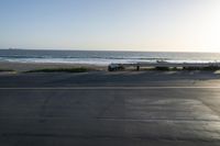 an empty road near a beach and waves as well as cars on the sand and houses on the beach