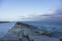 a sea wall lined with rocks sitting next to the ocean in front of the water