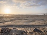 a sunset over the beach as people walk on sand and rocks in the water are visible