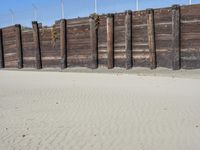 a fence that is next to some sand and a dirt field with two people on it