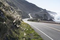 the coast highway in california is winding with a single car driving along it and large cliff behind it