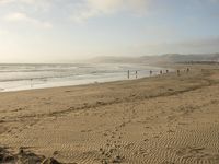 a beach is seen with people walking on it and the ocean is behind them and one person on the sand