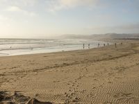 a beach is seen with people walking on it and the ocean is behind them and one person on the sand