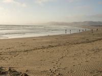 a beach is seen with people walking on it and the ocean is behind them and one person on the sand