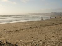 a beach is seen with people walking on it and the ocean is behind them and one person on the sand