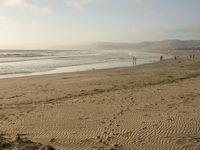 a beach is seen with people walking on it and the ocean is behind them and one person on the sand