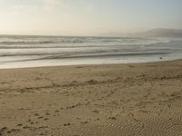 a beach is seen with people walking on it and the ocean is behind them and one person on the sand