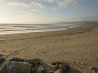 a beach is seen with people walking on it and the ocean is behind them and one person on the sand