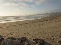 a beach is seen with people walking on it and the ocean is behind them and one person on the sand