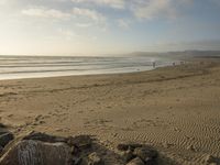 a beach is seen with people walking on it and the ocean is behind them and one person on the sand