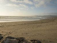 a beach is seen with people walking on it and the ocean is behind them and one person on the sand