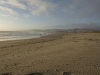 a beach is seen with people walking on it and the ocean is behind them and one person on the sand