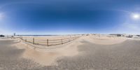 a fisheye lens on an empty beach with cars parked on the sand and in the distance a road with buildings and sand dunes