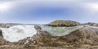 a 360 - lens image of the ocean and rocks on the shore of a beach