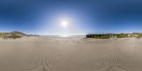 a panorama of a beach with the sun shining above it and some sand dunes to the side