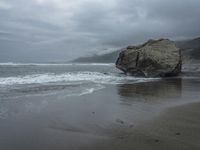 this person is walking on a beach in the rain near the ocean and large rocks