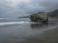 this person is walking on a beach in the rain near the ocean and large rocks