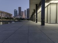 the walkway at the park leads to a lake and buildings in the background as evening falls