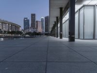 the walkway at the park leads to a lake and buildings in the background as evening falls