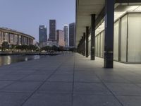 the walkway at the park leads to a lake and buildings in the background as evening falls