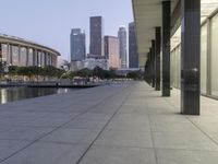 the walkway at the park leads to a lake and buildings in the background as evening falls