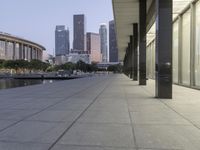 the walkway at the park leads to a lake and buildings in the background as evening falls