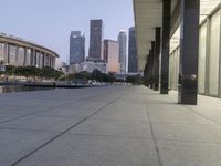 the walkway at the park leads to a lake and buildings in the background as evening falls