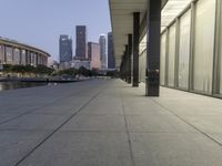 the walkway at the park leads to a lake and buildings in the background as evening falls