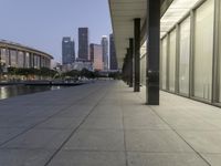 the walkway at the park leads to a lake and buildings in the background as evening falls