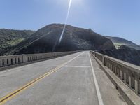 a paved bridge with a mountain in the back ground with an orange caution line on the right