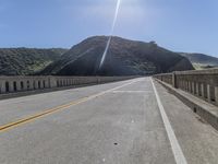 a paved bridge with a mountain in the back ground with an orange caution line on the right