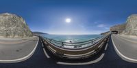 a fish eye view of an ocean bridge near the beach and the cliffs above it