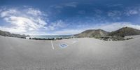 fish eye view of a city with lots of houses on a hill side road and mountains and ocean in the background