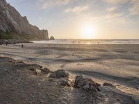 people walking on the beach at sunset next to a rocky cliff covered in sand and a body of water