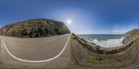 a fish eye view of the road going down to the ocean next to a large cliff