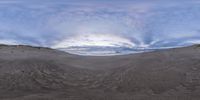 a fish eye view of an empty sandy area with hills in the background and a cloudy sky