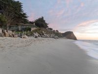 a large house sitting above a cliff at the beach next to the ocean with trees