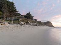 a large house sitting above a cliff at the beach next to the ocean with trees