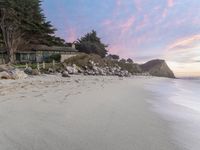 a large house sitting above a cliff at the beach next to the ocean with trees