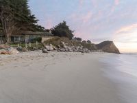 a large house sitting above a cliff at the beach next to the ocean with trees