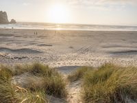 a beach with grass and sand with the sun setting above it as the sky passes