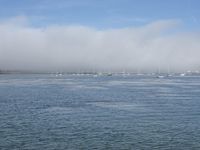 many small boats traveling on a very still calm blue sea with mist coming off the horizon