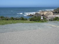 an empty parking lot near the ocean with a sign in the foreground reading no parking and beach next to them