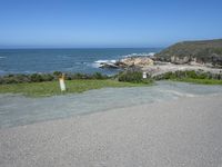 an empty parking lot near the ocean with a sign in the foreground reading no parking and beach next to them