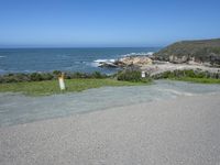 an empty parking lot near the ocean with a sign in the foreground reading no parking and beach next to them