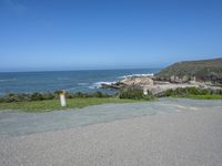 an empty parking lot near the ocean with a sign in the foreground reading no parking and beach next to them