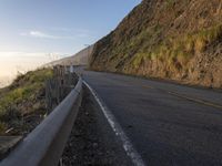 a long road passing by a mountain side and a hillside at sunset with a car driving on it