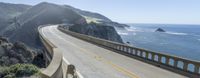 a person rides down the top of a bridge near the ocean and mountains on their bike